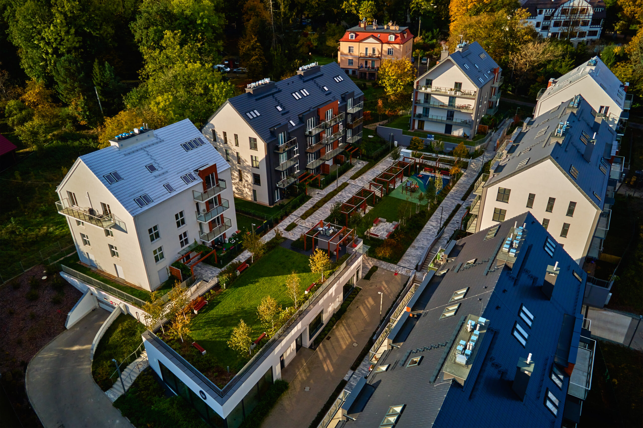 Aerial view of modern residential neighborhood with contemporary apartment buildings, green spaces, parking areas and well-maintained pathways on sunny day