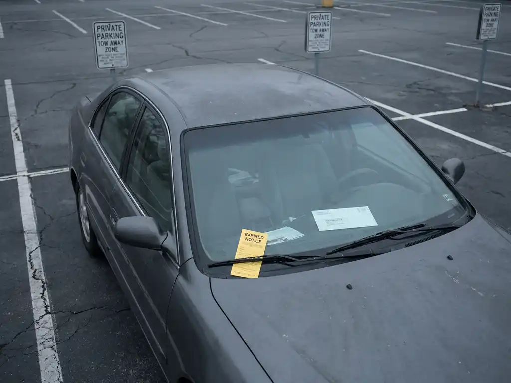 Auto mit abgelaufenem Parkschein unter dem Scheibenwischer und Einschreiben auf dem Armaturenbrett in privatem Parkplatz.