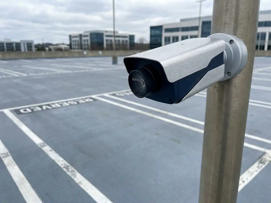 Automatische Kennzeichenerkennungskamera auf einem Parkplatzpfosten scannt einen leeren reservierten Stellplatz mit weißen Markierungen.