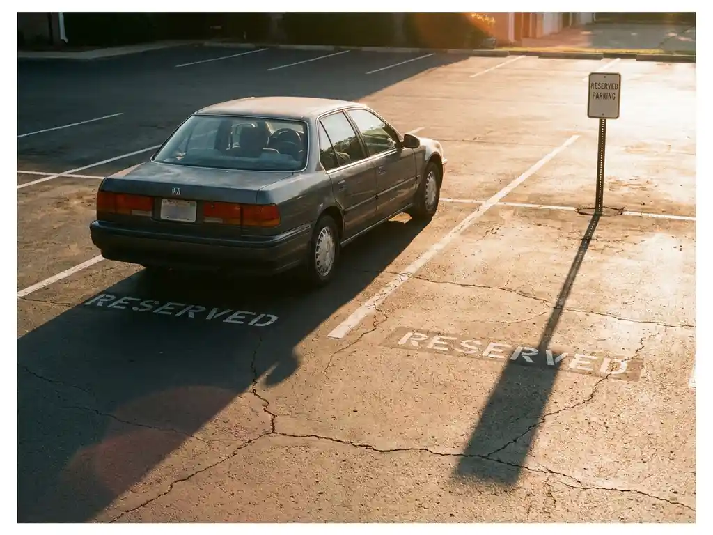 Auto parkt illegal über zwei reservierte Stellplätze in einem städtischen Parkplatz, goldenes Nachmittagslicht auf weißen Markierungen.