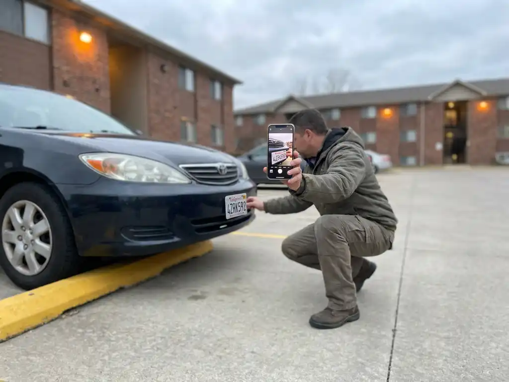 Hausverwalterin fotografiert mit Smartphone das Kennzeichen eines falsch geparkten Autos auf einem Wohnanlage-Parkplatz.