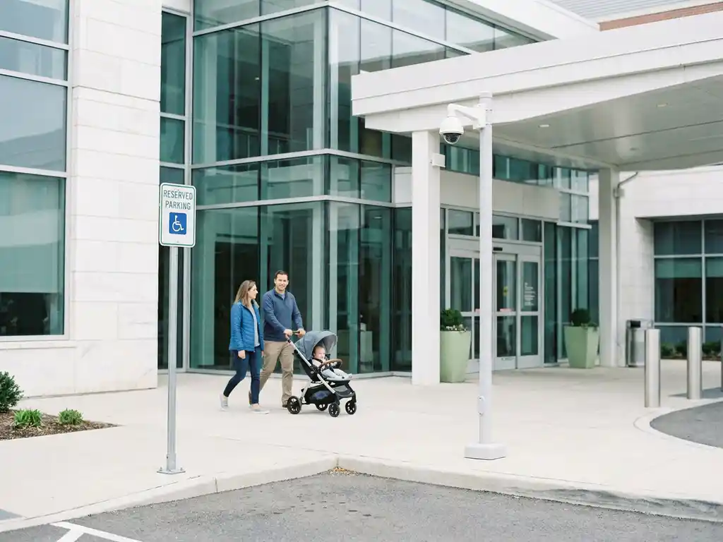Reservierter Parkplatz vor einem modernen Krankenhauseingang mit Kamerasystem, Familie mit Kinderwagen kommt an.