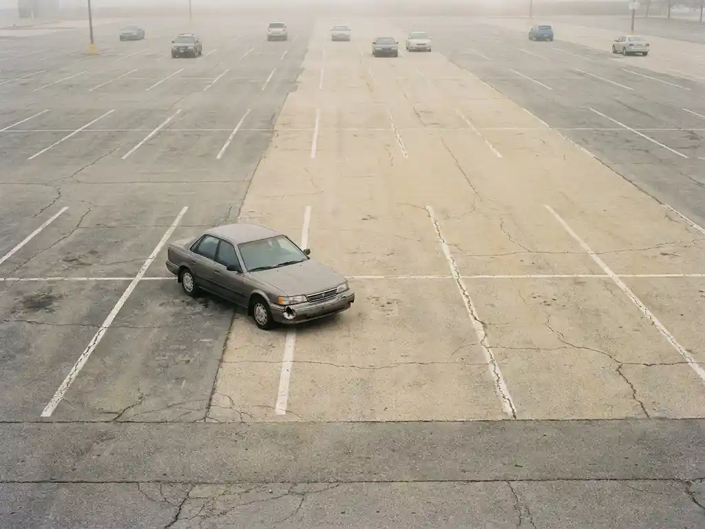 Einzelnes Auto parkt schräg über zwei Stellplätze in fast leerem Parkplatz mit verblassten weißen Markierungen.