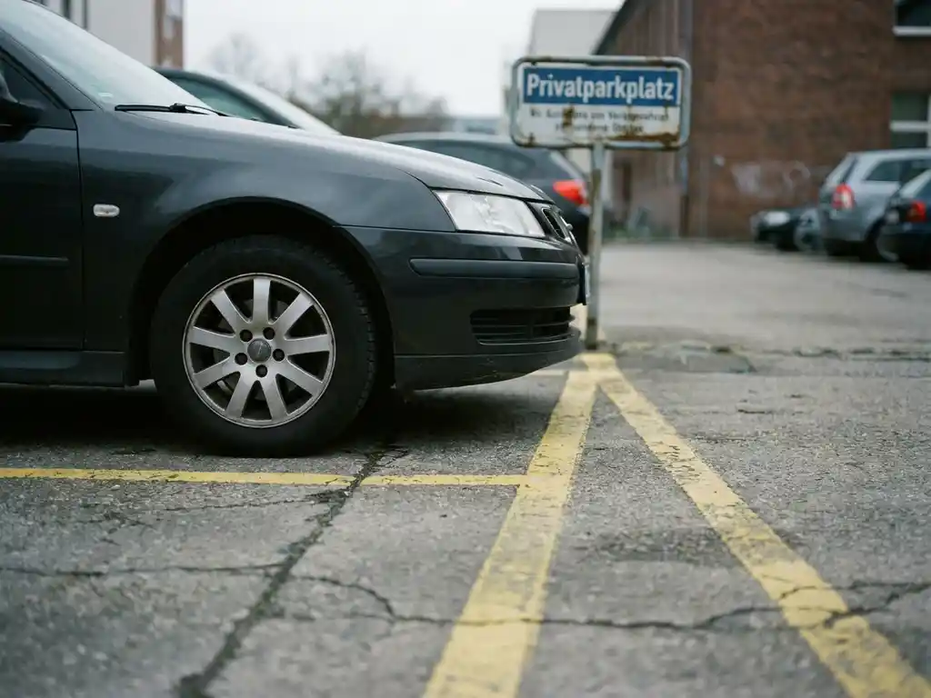 Auto parkt regelwidrig über zwei markierte Stellplätze auf einem Privatparkplatz mit gelbem Bodenmarkierungen.